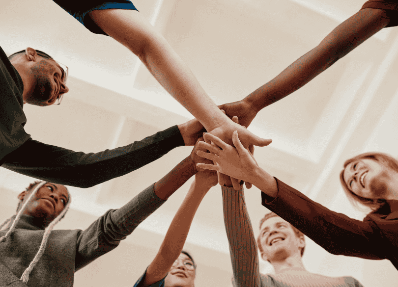 Várias pessoas em círculo com as mãos sobrepostas ao centro, simbolizando uma equipe motivada.